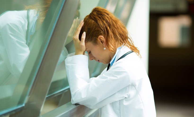 stressed female doctor in white medical coat pressing her head against a glass...