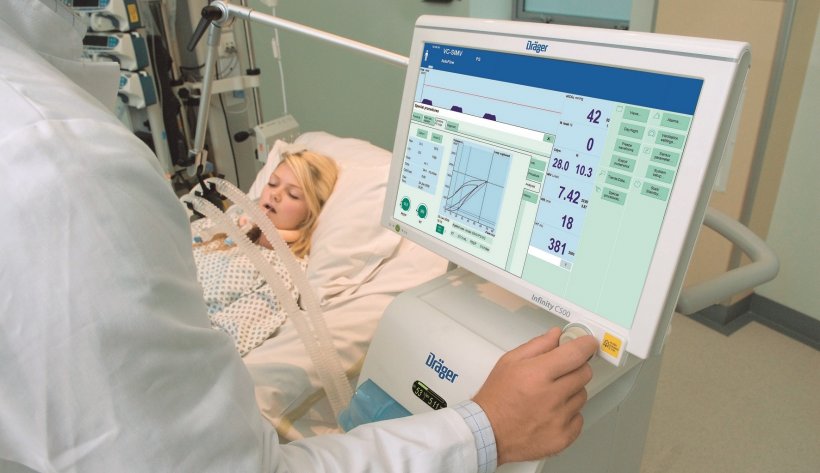 doctor operating touchscreen of a ventilation device next to a hospital patient