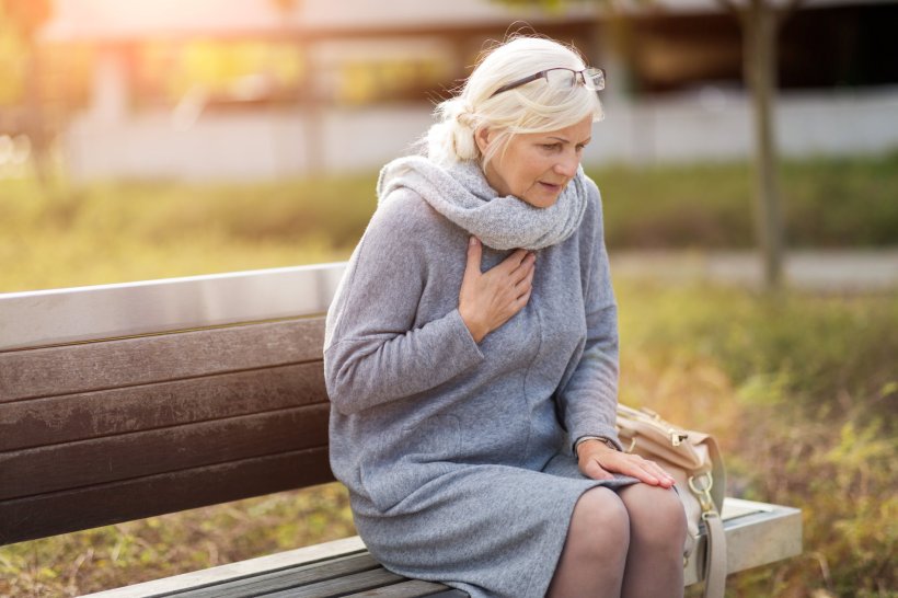 distressed looking older woman sitting on wooden bench with her hand on her...