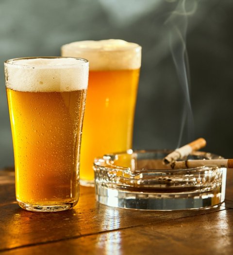 two chilled beer glasses standing next to ashtray with burning cigarettes